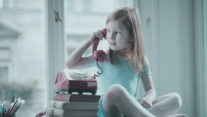 A child speaking with an old style telephone to her ear